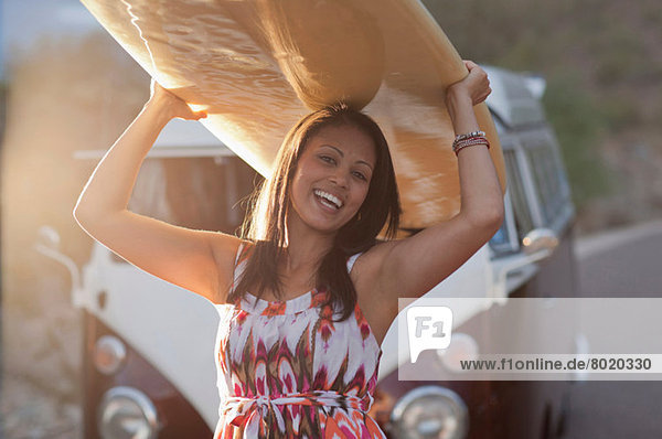 Junge Frau mit Surfbrett auf Roadtrip  lächelnd
