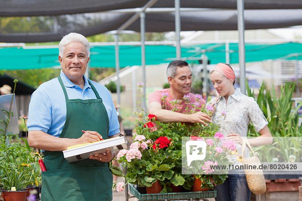 Senior Gärtner mit Zwischenablage mit Kunden im Hintergrund des Gartencenters