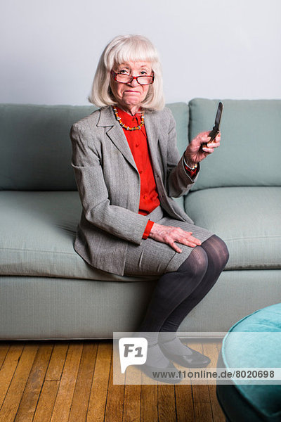 Senior woman sitting on sofa holding mobile phone