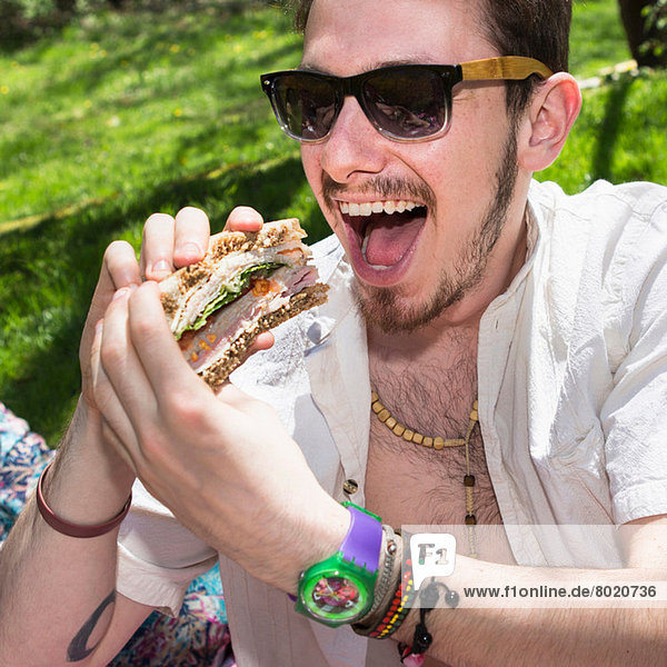 Mann mit Sonnenbrille isst Sandwich