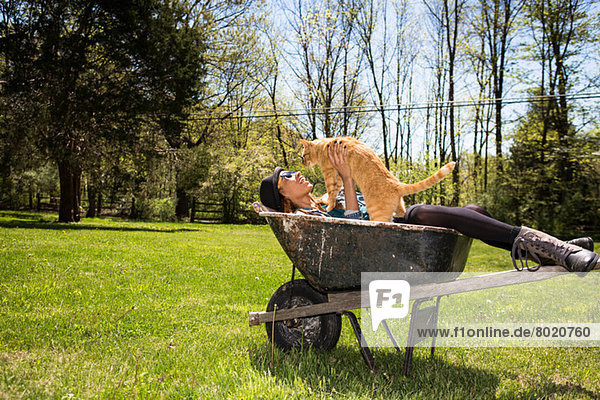 Woman in wheelbarrow holding ginger cat