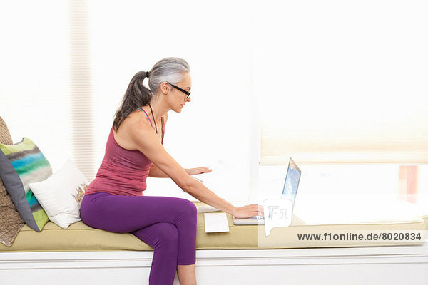 Frau sitzt auf Fensterbank mit Laptop