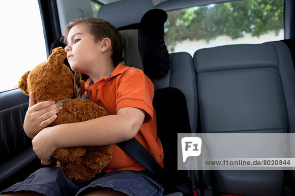 Junge schaut aus dem Autofenster und hält einen Teddybären.