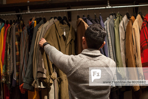 Junger Mann schaut durch die Kleiderstange im Vintage-Shop