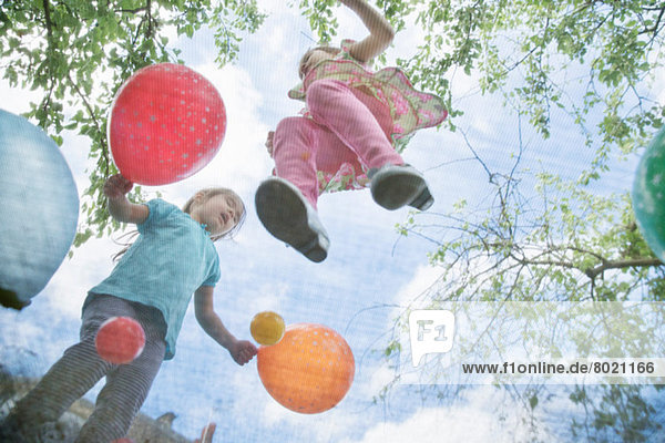 Junge Mädchen beim Springen auf Gartentrampolin mit Luftballons