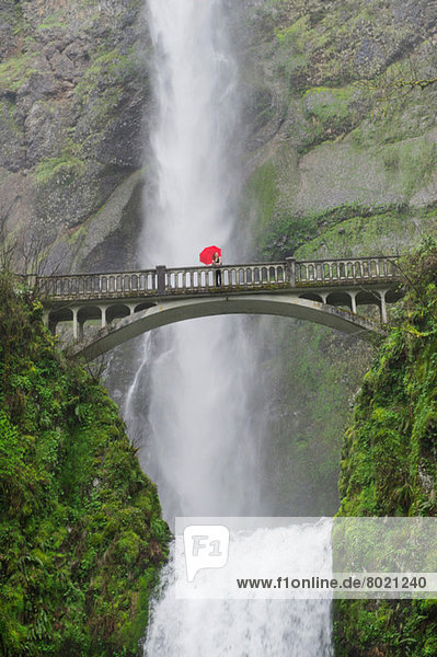 Woman with red umbrella on footbridge over Multnomah Falls  Columbia River Gorge  USA