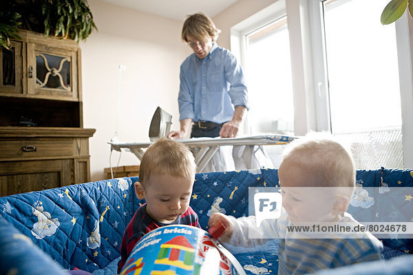 Junger Vater bei der Hausarbeit während seine Söhne im Laufgitter spielen