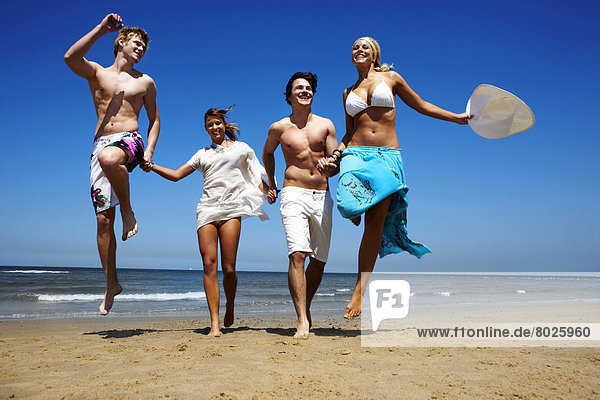 Two young man and two young women are jumping on the beach.