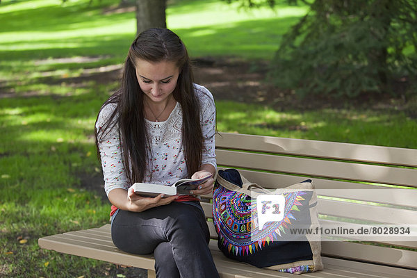 Young woman reading in a park sitting on a park bench Edmonton alberta canada