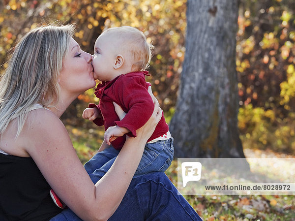 Portrait of a mother kissing her baby daughter in a park in autumn Edmonton alberta canada