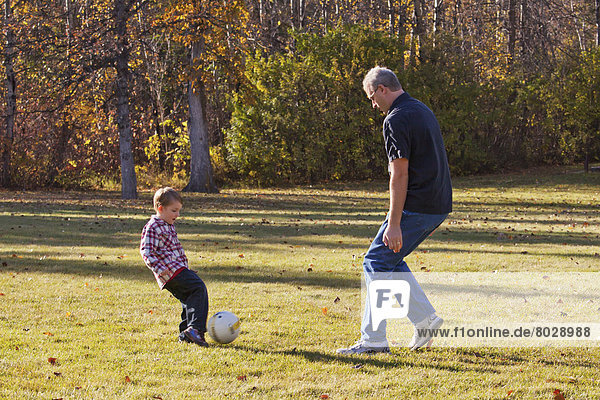 Grandfather and grandson playing soccer in a park in autumn Edmonton alberta canada