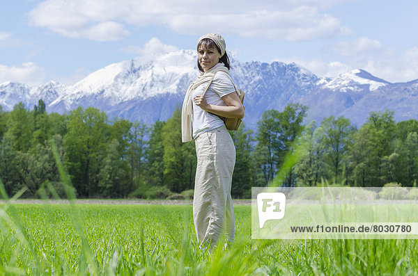 A woman stands in a grass field with the alps mountain range in the background Locarno ticino switzerland