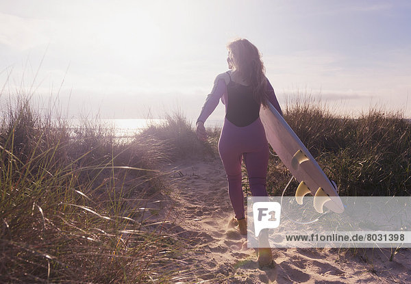 A woman carries her surfboard down a sandy path to the beach Tarifa cadiz andaulsia spain