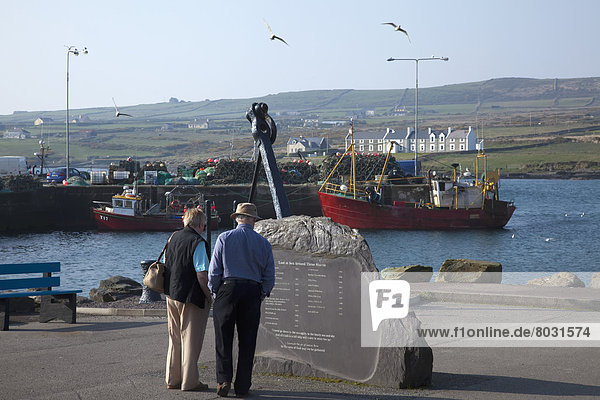 A senior couple reads a plaque at the harbour Portmagee county kerry ireland