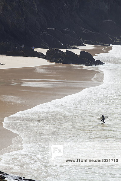 A surfer carries his surfboard out of the water at coomenoole beach near dunquin County kerry ireland