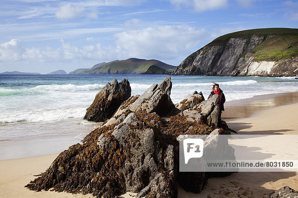 A woman stands on a rock formation on coomenoole beach near dunquin at the coast County kerry ireland
