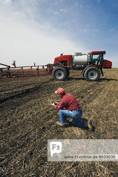 A Man Examines Newly Seeded Soil Next To A High Clearance Sprayer Being Used To Apply Liquid Fertilizer  Near Dugald  Manitoba  Canada
