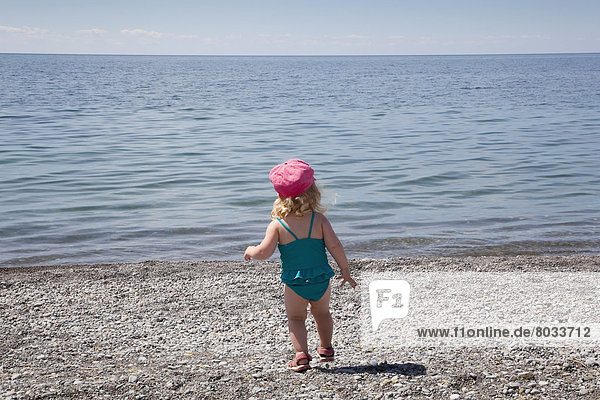 Young girl running on a pebble beach by the shore of lake ontario Ontario canada