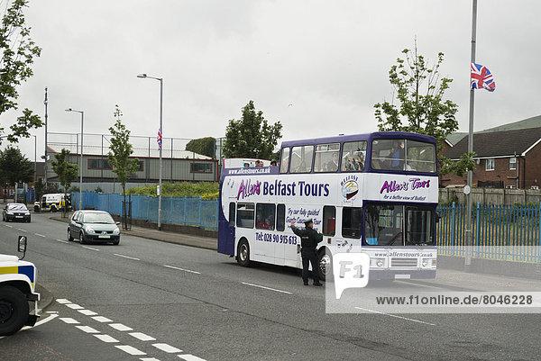 Policeman stopping double decker tour bus in loyalist sector of city  Belfast  Northern Ireland  United Kingdom