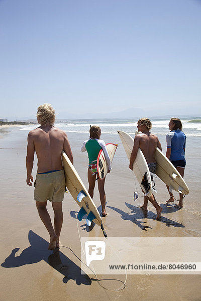 South Africa  Surfers walking beach carrying boards  Mossel Bay