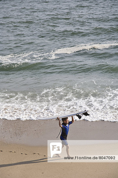 USA  Rhode Island  Boy walking beach carrying surfboard on head  Newport