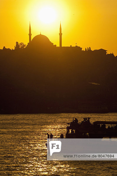 Ferry crossing Golden Horn with silhouette of Eyup Sultan Mosque behind at dusk  Istanbul  Turkey