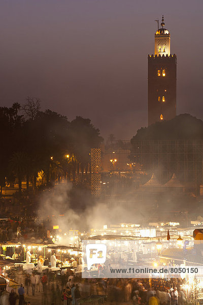 Looking across food stalls in Dejmaa el Fna at dusk with minaret of Koutoubia Mosque behind  Marrakesh  Morocco