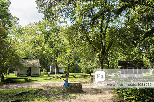 Girl standing by well near slave cabins in Oakley Plantation Audubon State Historic Site  Louisiana  USA