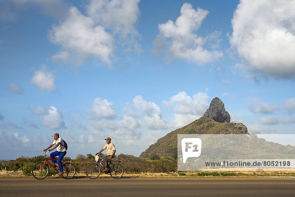 Cyclists and Morro do Pico in background  Fernando de Noronha  Pernambuco  Brazil