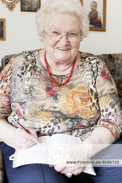 Lächelnde alte Frau mit Brille schreibt