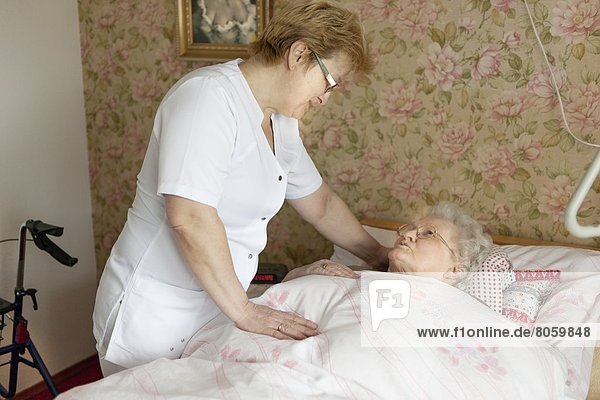Altenpflegerin spricht mit alter Frau im Bett