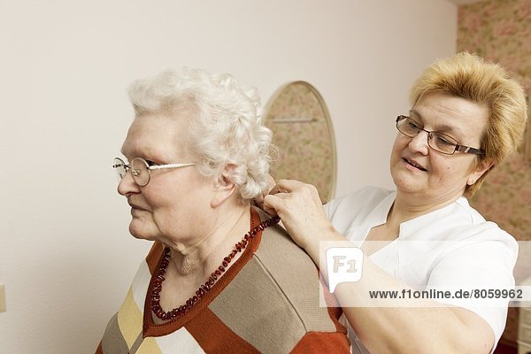 Altenpflegerin hängt alter Frau ihre Kette um