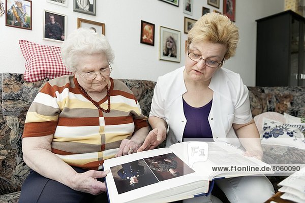 Altenpflegerin und alte Frau schauen in ein Fotoalbum