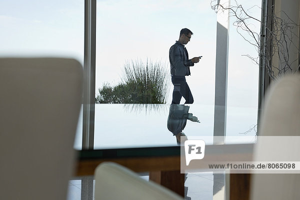 Businessman using cell phone at office window