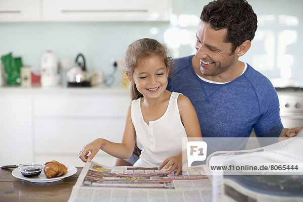 Vater und Tochter lesen Zeitung beim Frühstück