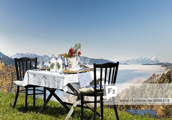 Gedeckter Tisch im Landhaus-Stil auf einer Almwiese mit Alpenpanorama