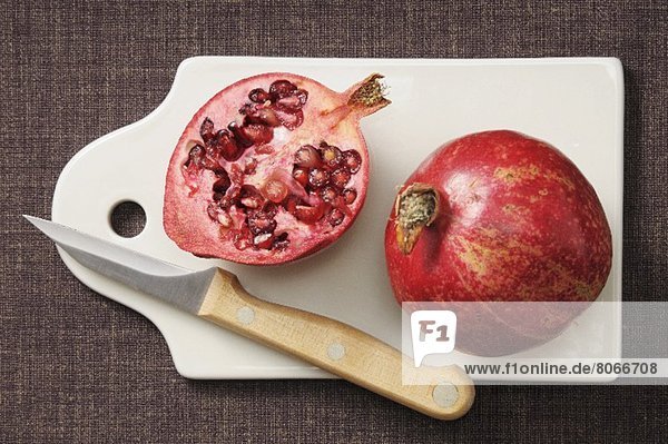 Ganzer und halber Granatapfel auf Schneidebrett mit Messer