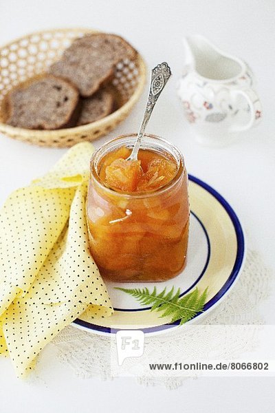 Geöffnetes Glas Melonenmarmelade mit Löffel vor Brotkorb