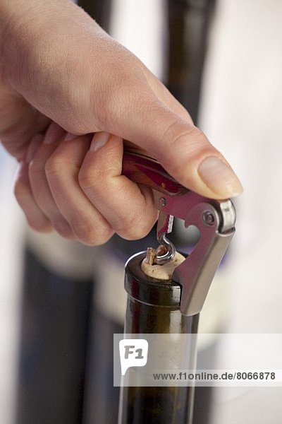 A bottle of red wine being opened with a corkscrew