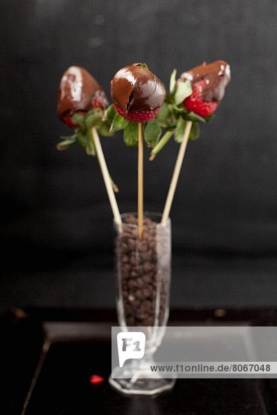 Drei Schokoladenerdbeeren auf Spiessen in einem Glas mit Chocolatechips
