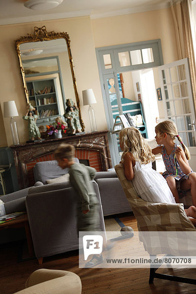 Three children playing in a house: two lgirls looking at the boy. Out of focus motion  family  children  brother  sister