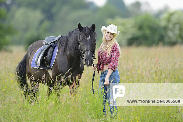 Junge Frau steht neben einem Pferd auf einer Wiese