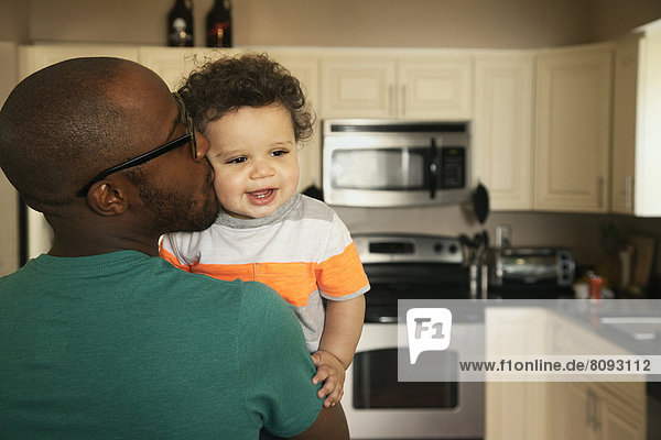 Father kissing baby in kitchen