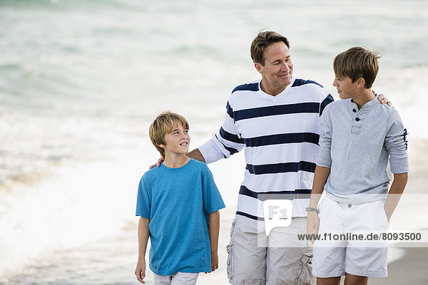 Caucasian father and sons walking on beach