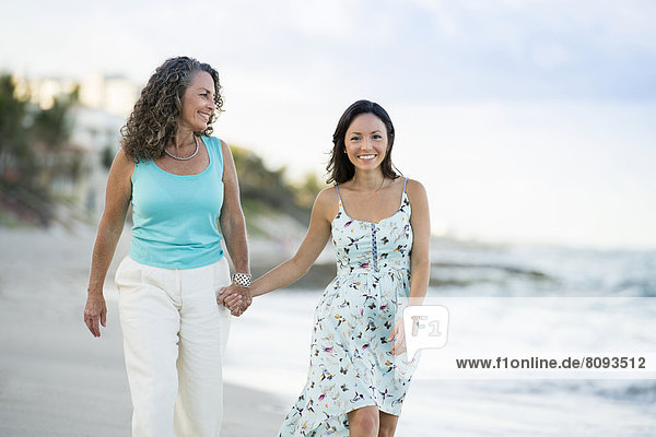 Caucasian mother and daughter walking on beach