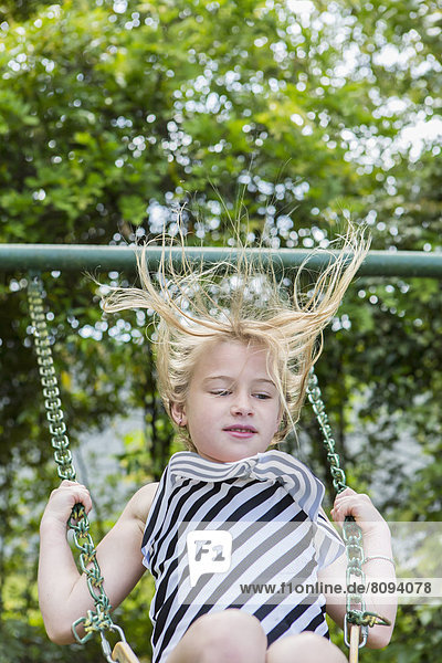 Caucasian girl playing on swing in park