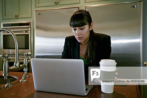 Mixed race businesswoman using laptop in kitchen