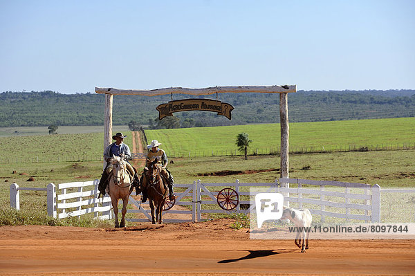 Two men riding horses  cowboys  entrance of a fazenda or ranch of a landowner