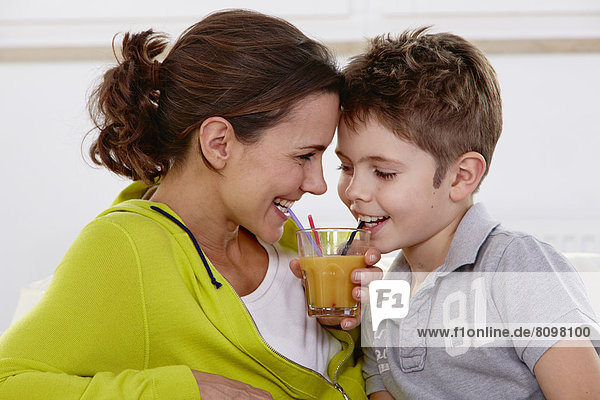 Mutter und Sohn trinken aus einem gemeinsamen Glas Saft