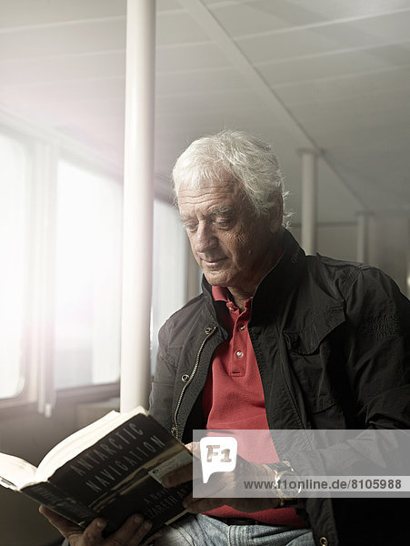 Älterer Mann liest ein Buch auf einem Schiff